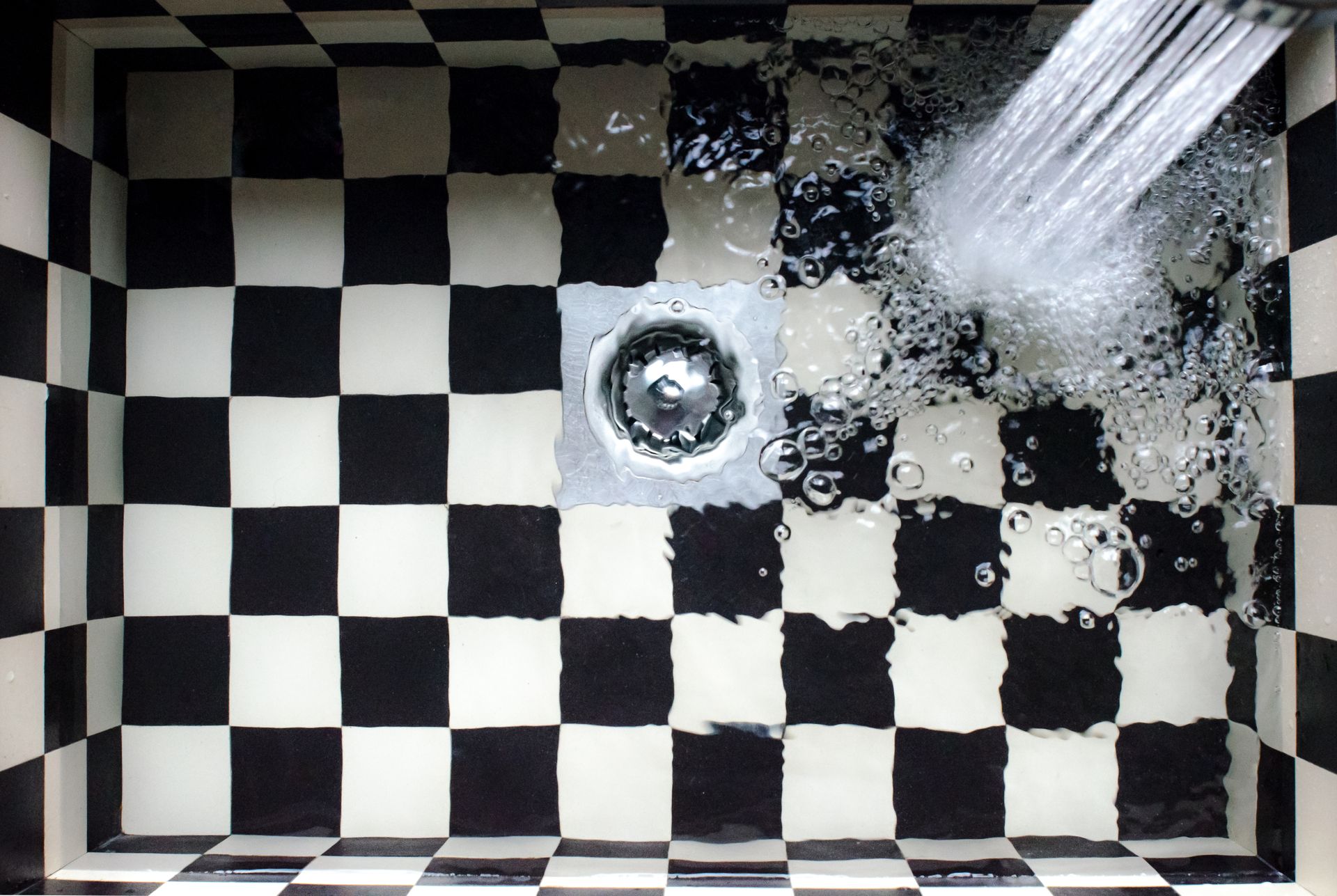 black and white checkboard sink with water running and drain clog