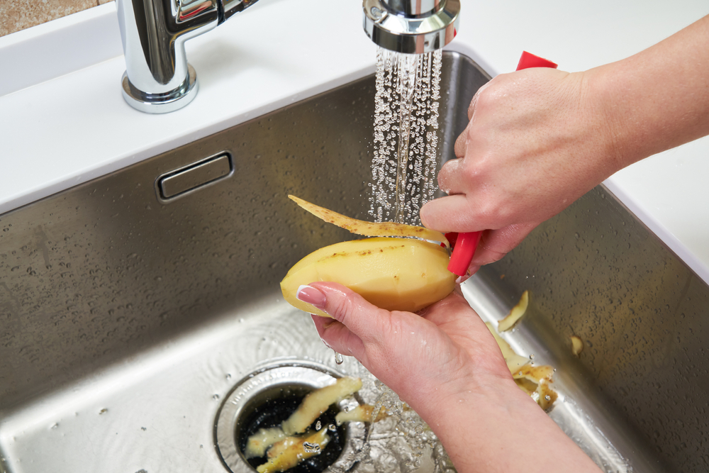 woman peeling a potato above a garbage disposal drain